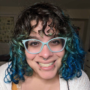a woman with shoulder length green and blue hair offering a wide smile